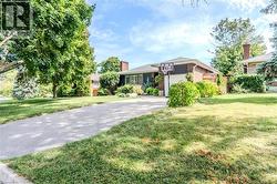 View of front of house featuring a front yard, a chimney, brick siding, and driveway - 