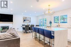 Kitchen featuring open floor plan, a kitchen breakfast bar, decorative light fixtures, a glass covered fireplace, and white cabinetry - 