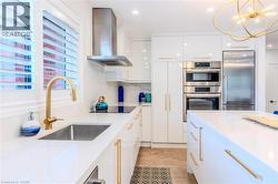 Kitchen with wall chimney range hood, appliances with stainless steel finishes, hanging light fixtures, white cabinets, and light stone countertops - 