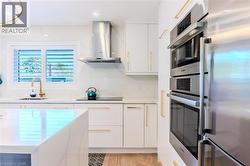 Kitchen featuring appliances with stainless steel finishes, modern cabinets, white cabinets, wall chimney exhaust hood, and light stone counters - 