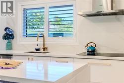 Kitchen view of exhaust hood, white cabinetry, light stone countertops, black electric cooktop, and modern cabinets - 