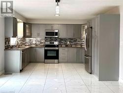 Kitchen with gray cabinetry, appliances with stainless steel finishes, dark countertops, and marble finish floor - 