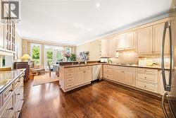 Kitchen with ornamental molding, a peninsula, dark stone countertops, cream cabinetry, and dark wood finished floors - 