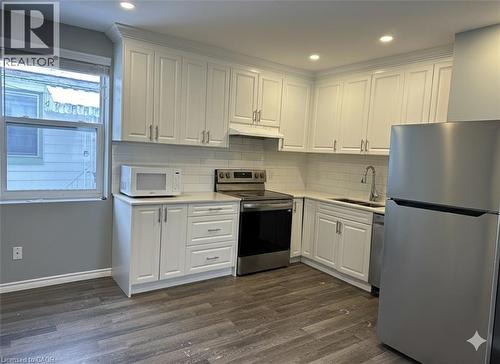 Kitchen featuring stainless steel appliances, white cabinets, dark wood-style flooring, decorative backsplash, and under cabinet range hood - 80 Glen Road Unit# Upper, Kitchener, ON - Indoor Photo Showing Kitchen With Double Sink