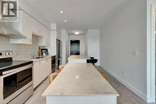 Kitchen with wall chimney exhaust hood, stainless steel electric range oven, a kitchen island, freestanding refrigerator, and white cabinets - 15 Glebe Street Unit# 1511, Cambridge, ON - Indoor Photo Showing Kitchen With Upgraded Kitchen