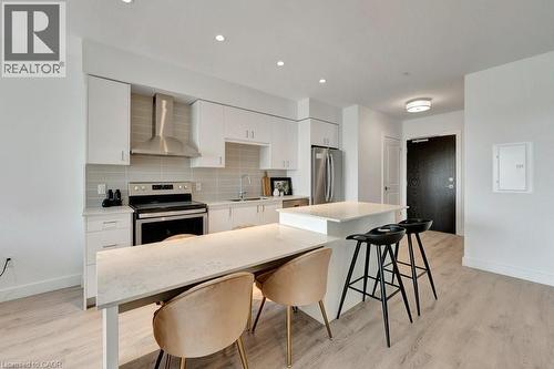 Kitchen with wall chimney range hood, stainless steel appliances, light wood finished floors, tasteful backsplash, and white cabinetry - 15 Glebe Street Unit# 1511, Cambridge, ON - Indoor Photo Showing Kitchen With Upgraded Kitchen
