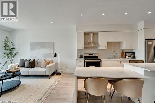 Kitchen with wall chimney range hood, appliances with stainless steel finishes, white cabinets, light wood finished floors, and decorative backsplash - 15 Glebe Street Unit# 1511, Cambridge, ON - Indoor
