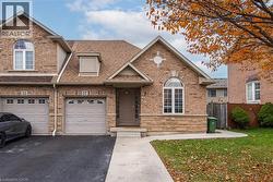 View of front facade with driveway, roof with shingles, stone siding, a garage, and brick siding - 