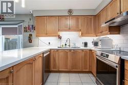 Kitchen featuring appliances with stainless steel finishes, backsplash, under cabinet range hood, light tile patterned flooring, and brown cabinetry - 