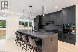 Kitchen featuring a breakfast bar, a kitchen island with sink, modern cabinets, tasteful backsplash, and hanging light fixtures - 