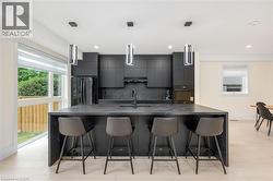 Kitchen featuring a breakfast bar, a large island, black appliances, hanging light fixtures, and recessed lighting - 