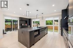 Kitchen featuring modern cabinets, decorative light fixtures, dark stone counters, a center island with sink, and light wood finished floors - 