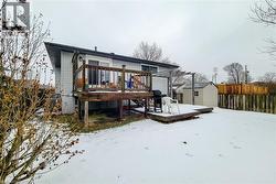 Snow covered rear of property featuring a storage unit, a wooden deck, and a fenced backyard - 