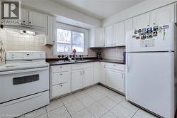 Kitchen featuring white appliances, dark countertops, under cabinet range hood, white cabinetry, and light tile patterned floors - 