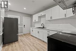 Kitchen with black electric range oven, custom exhaust hood, white cabinets, freestanding refrigerator, and wainscoting - 