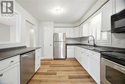 Kitchen with appliances with stainless steel finishes, dark countertops, white cabinets, and light wood-style flooring - 