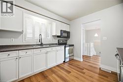 Kitchen featuring stainless steel appliances, dark countertops, white cabinets, and light wood-style flooring - 