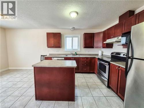 Kitchen with reddish brown cabinets, stainless steel appliances, a textured ceiling, a kitchen island, and under cabinet range hood - 132 Udvari Crescent Unit# 3, Kitchener, ON - Indoor Photo Showing Kitchen With Double Sink