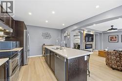 Kitchen with dark brown cabinetry, open floor plan, stainless steel appliances, a center island with sink, and light wood finished floors - 