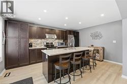 Kitchen featuring dark brown cabinetry, a breakfast bar, a center island with sink, stainless steel appliances, and under cabinet range hood - 