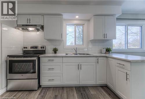 Kitchen with stainless steel electric range oven, under cabinet range hood, white cabinets, a peninsula, and dark wood finished floors - 156 Donald Street, Kitchener, ON - Indoor Photo Showing Kitchen With Stainless Steel Kitchen With Double Sink