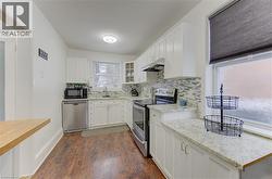 Kitchen featuring appliances with stainless steel finishes, white cabinets, glass insert cabinets, under cabinet range hood, and dark wood finished floors - 