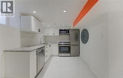 Kitchen featuring white cabinets, appliances with stainless steel finishes, light stone countertops, decorative backsplash, and light marble finish flooring - 