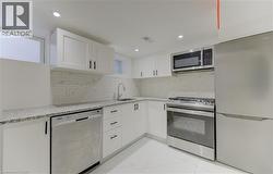 Kitchen featuring stainless steel appliances, white cabinets, light stone counters, decorative backsplash, and light marble finish flooring - 