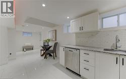 Kitchen featuring white cabinets, light stone counters, stainless steel dishwasher, decorative backsplash, and open floor plan - 