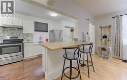 Kitchen featuring a breakfast bar, stainless steel appliances, white cabinetry, dark wood-type flooring, and crown molding - 