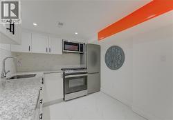 Kitchen with light stone countertops, appliances with stainless steel finishes, white cabinetry, recessed lighting, and tasteful backsplash - 