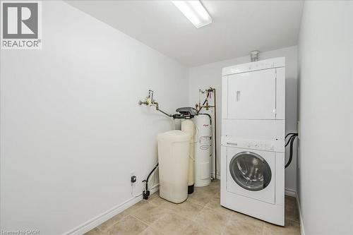 Laundry room featuring stacked washing machine and dryer, light tile patterned floors, and water heater - 41 Goodwin Drive Unit# 202, Guelph, ON - Indoor Photo Showing Laundry Room