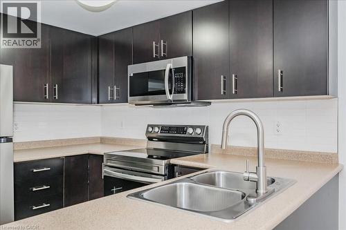 Kitchen with appliances with stainless steel finishes, backsplash, light countertops, and dark brown cabinets - 41 Goodwin Drive Unit# 202, Guelph, ON - Indoor Photo Showing Kitchen With Double Sink