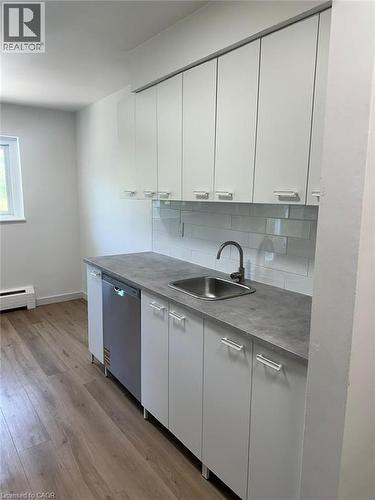 Kitchen with tasteful backsplash, baseboard heating, dishwasher, light wood-type flooring, and white cabinets - 145 Macgregor Crescent Unit# 1, Waterloo, ON - Indoor Photo Showing Kitchen