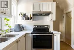 Kitchen featuring stainless steel electric range, tasteful backsplash, white cabinetry, and under cabinet range hood - 