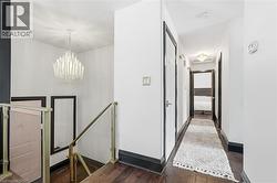 Hall featuring an upstairs landing, a chandelier, and dark wood-style flooring - 