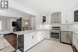 Kitchen featuring stainless steel appliances, glass insert cabinets, light stone counters, wall chimney exhaust hood, and recessed lighting - 