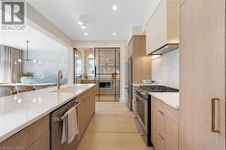 Kitchen featuring modern cabinets, premium appliances, light brown cabinets, light stone counters, and recessed lighting - 