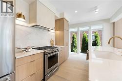 Kitchen featuring appliances with stainless steel finishes, decorative backsplash, light brown cabinets, light wood-style flooring, and modern cabinets - 