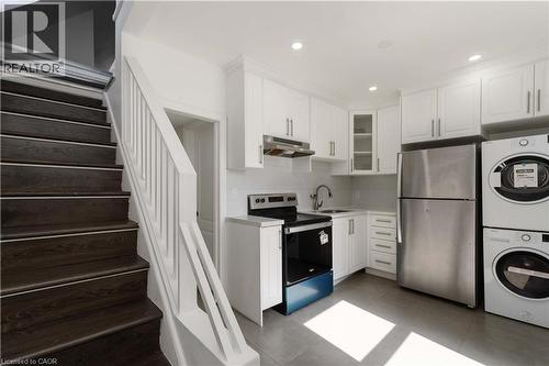 Kitchen featuring appliances with stainless steel finishes, light countertops, white cabinets, glass insert cabinets, and under cabinet range hood - 934 Barton Street E Unit# 2, Hamilton, ON - Indoor Photo Showing Laundry Room