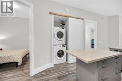 Laundry area behind barn door, light Laminate floors, and stacked washing machine and dryer - 