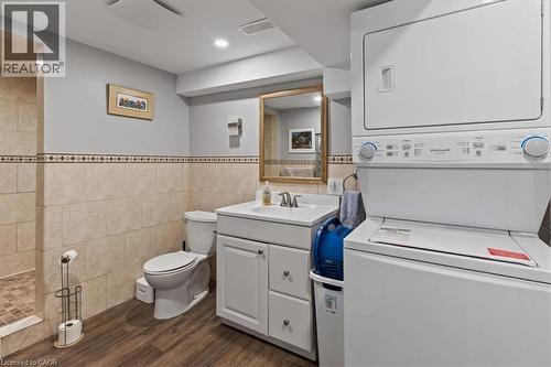 Full bath with vanity, dark wood-style floors, tile walls, stacked washing machine and dryer, and a tile shower - 50 Grove Crescent, Brantford, ON - Indoor Photo Showing Laundry Room