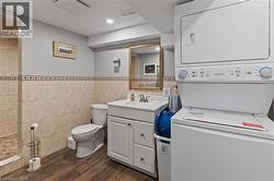 Full bath with vanity, dark wood-style floors, tile walls, stacked washing machine and dryer, and a tile shower - 