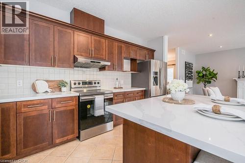Kitchen featuring appliances with stainless steel finishes, under cabinet range hood, light stone counters, light tile patterned flooring, and decorative backsplash - 609 Woolgrass Avenue, Waterloo, ON - Indoor Photo Showing Kitchen