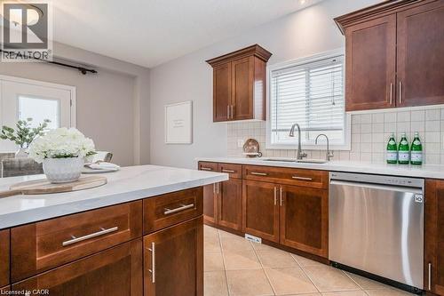 Kitchen with stainless steel dishwasher, light tile patterned floors, backsplash, light stone countertops, and brown cabinetry - 609 Woolgrass Avenue, Waterloo, ON - Indoor Photo Showing Kitchen