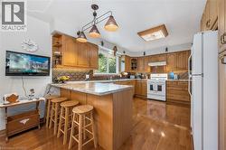 Kitchen with white appliances, a peninsula, dark wood-type flooring, and brown cabinets - 