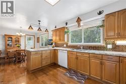 Kitchen featuring tasteful backsplash, dark wood finished floors, a chandelier, white dishwasher, and a peninsula - 