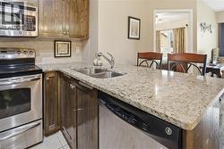 Kitchen featuring appliances with stainless steel finishes, a peninsula, light stone countertops, backsplash, and dark brown cabinets - 