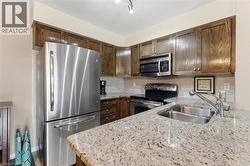 Kitchen with appliances with stainless steel finishes, light stone countertops, decorative backsplash, and dark brown cabinetry - 