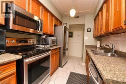 Kitchen with stainless steel appliances, brown cabinetry, decorative backsplash, light tile patterned floors, and light countertops - 